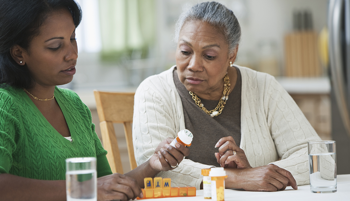 Adult daughter helping elderly mother review medications and pill organizer